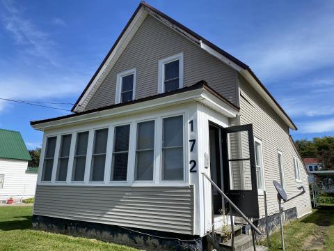 Image of one and a half story home with tan siding and sunporch
